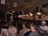 People seated at tables inside a restaurant. Dim lighting, multiple hanging lamps, and artwork on the walls.