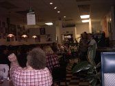 Restaurant interior with band playing, people seated at tables, checkered floor.