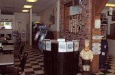 Interior of a restaurant with checkerboard floor, tables, a service counter, and a chef statue.