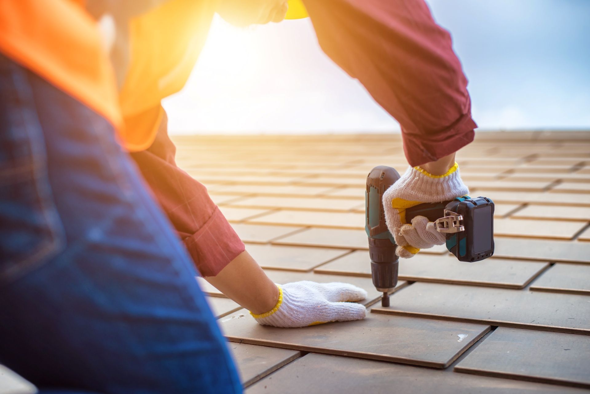 Person in gloves using a drill to install roof tiles on a sunny day.