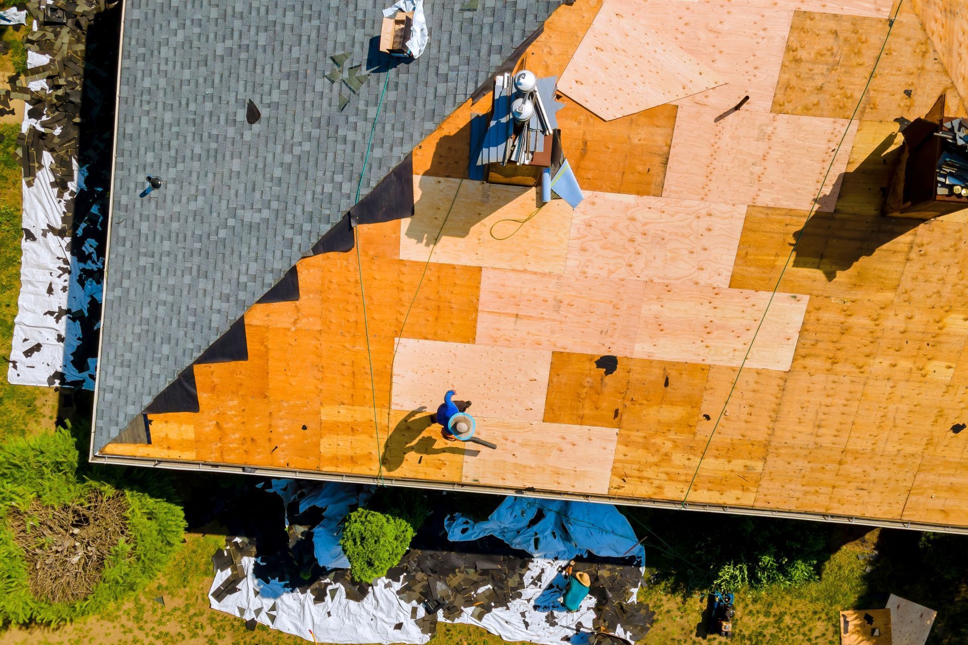 Aerial view of a roof under construction: worker, partially covered with new wood; old and new shingles.