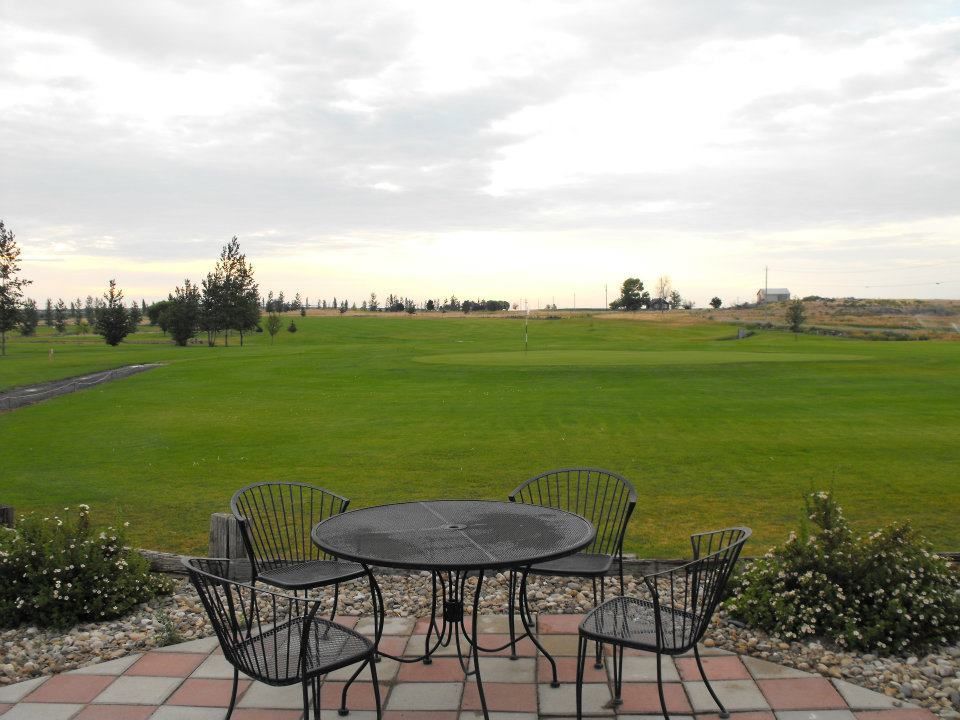 Patio table and chairs overlooking a wide green lawn under a cloudy sky