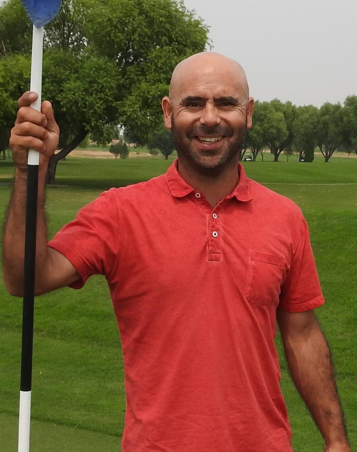 Smiling man in a red polo shirt holding a golf club on a green golf course