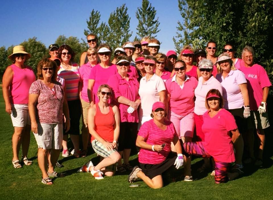 Group of people in bright pink shirts posing outdoors on a grassy field