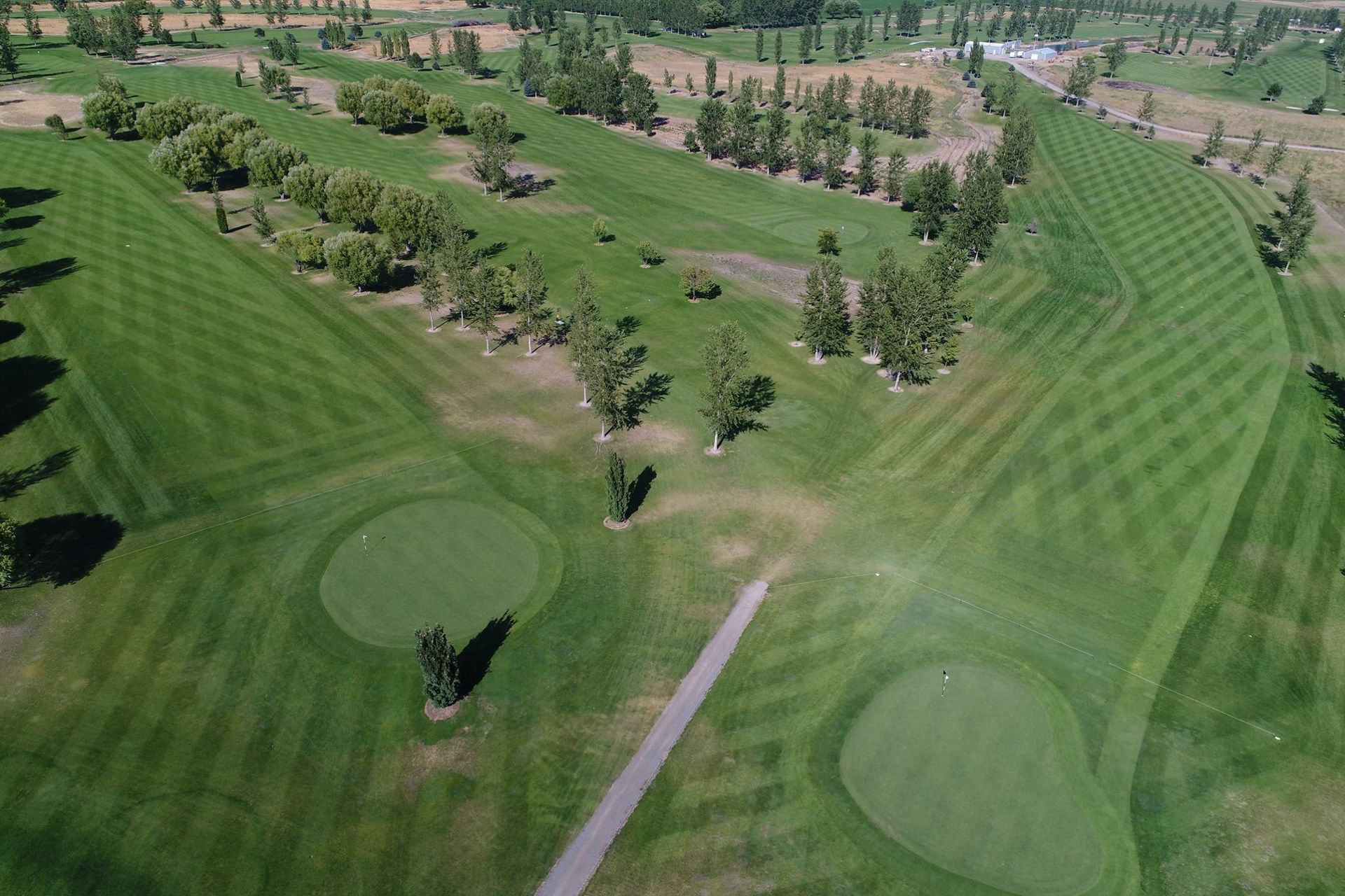 Aerial view of a golf course fairway with sand bunkers, trees, and a cart path on a sunny day
