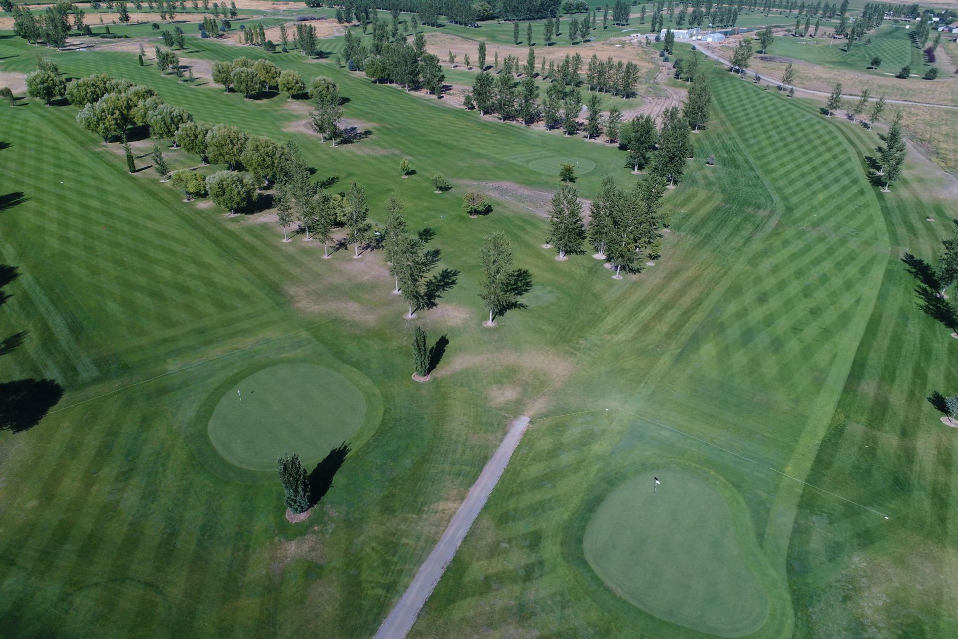 Aerial view of a golf course with green fairways, sand bunkers, and scattered trees.