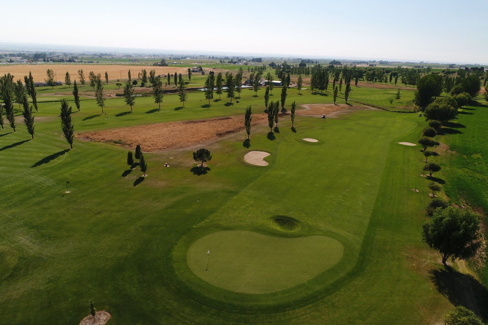 Aerial view of a lush golf course with fairway, sand bunkers, and scattered trees under clear skies