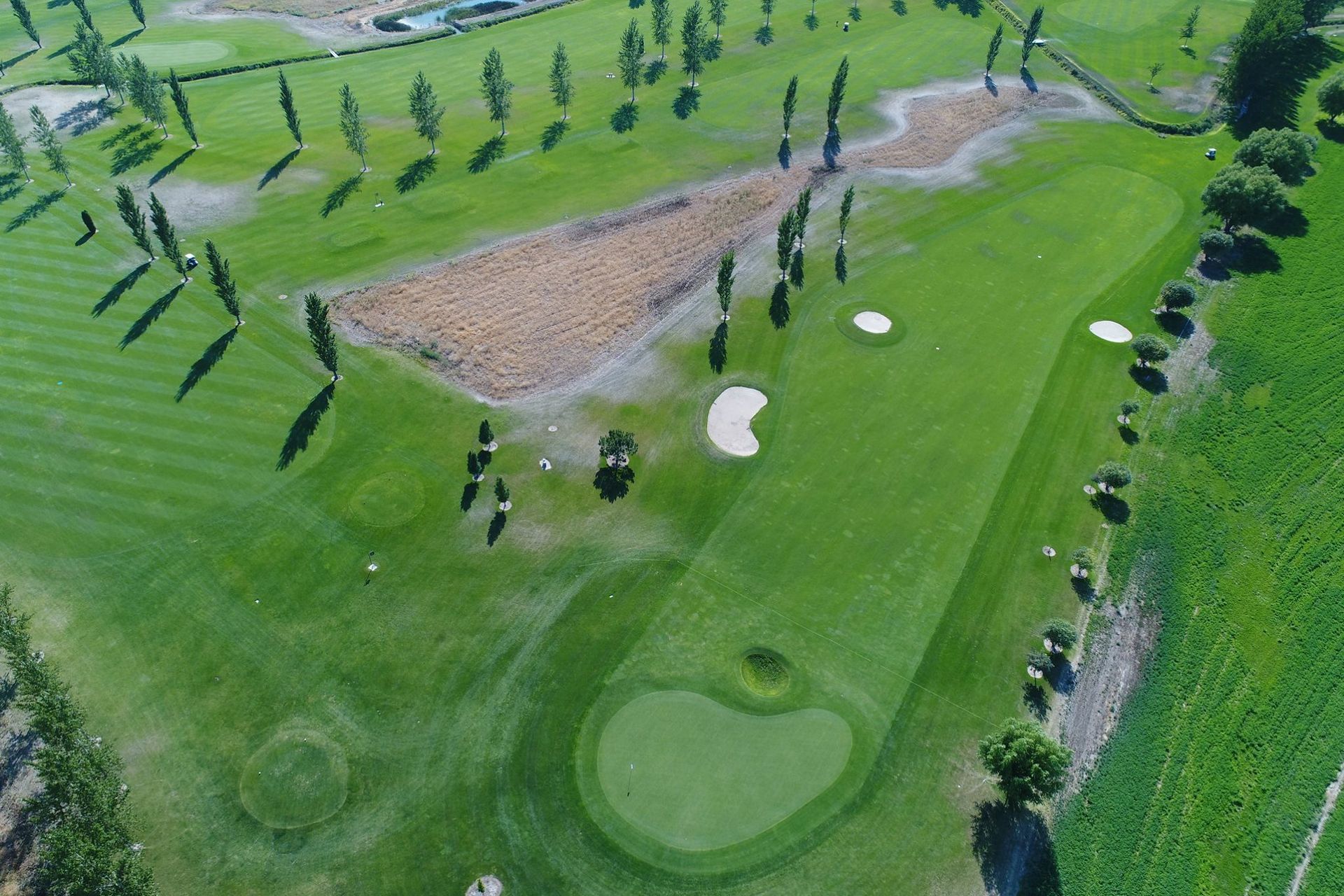 Aerial view of a green golf course with sand bunkers, fairways, and scattered trees.