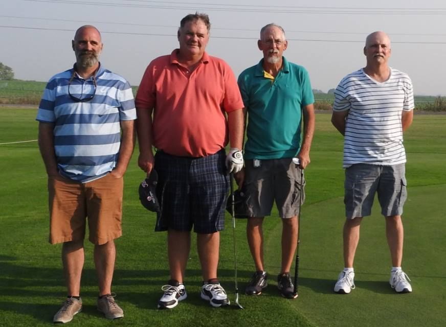 Four men standing on a golf course, wearing casual shirts and shorts.