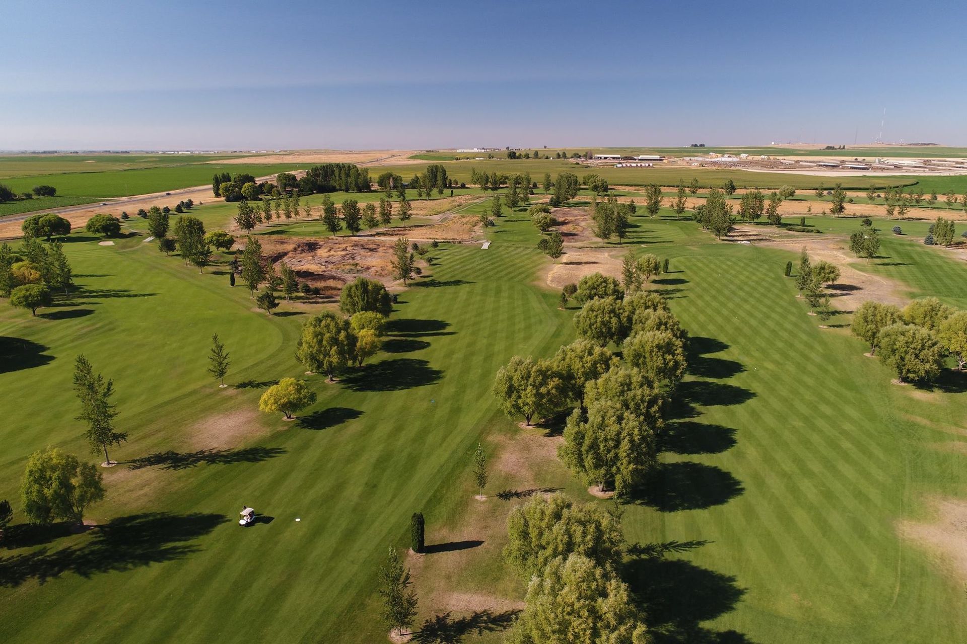 Aerial view of a green golf course with tree-lined fairways and sand bunkers under a clear sky