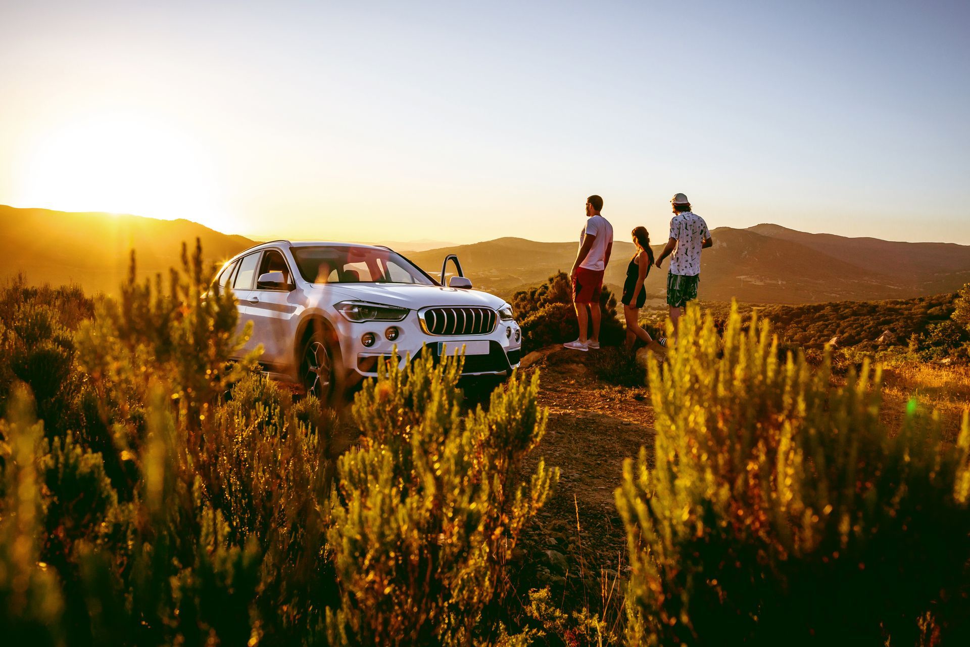 White SUV parked near three people viewing a mountain sunset. | Rocky Mountain Car Care