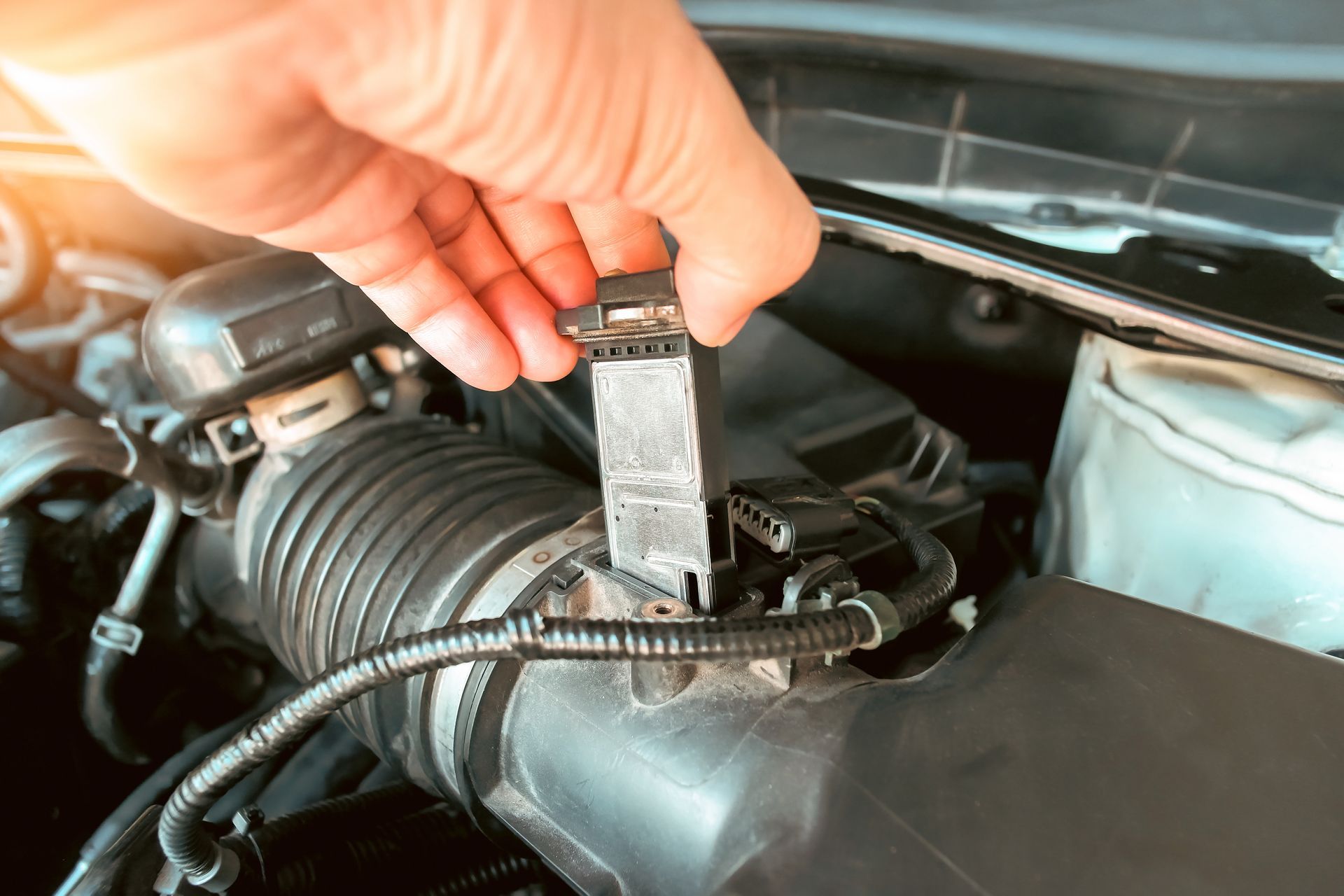 Hand removing a sensor from an engine's air intake system.  | Rocky Mountain Car Care