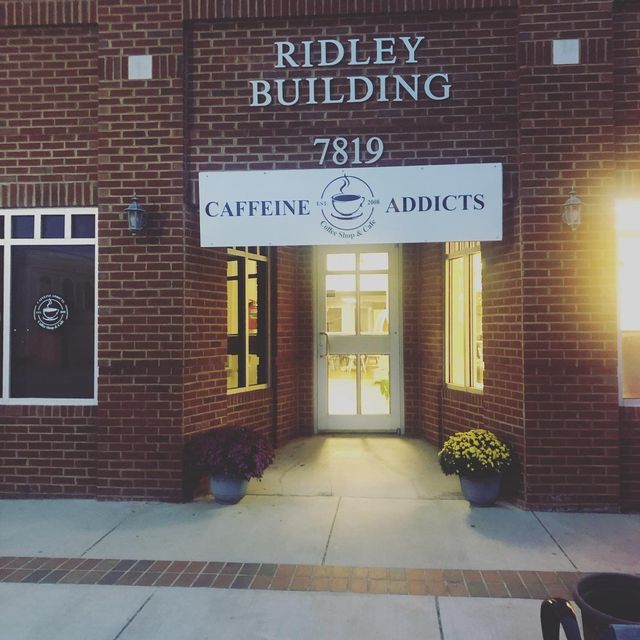 Exterior of "Caffeine Addicts" coffee shop in the Ridley Building, brick facade with an illuminated sign above the entrance, and address "7819".