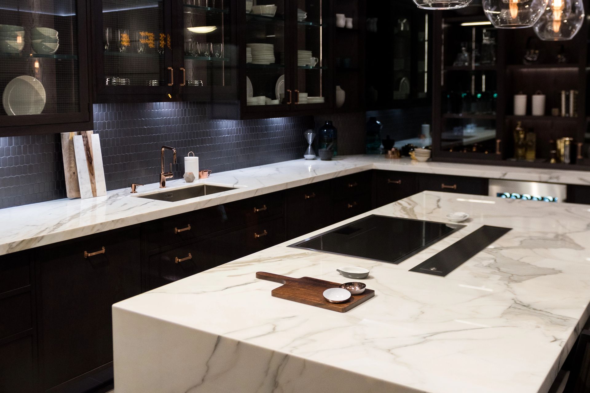 Cocina moderna con gabinetes oscuros, isla de mármol blanco y placa de cocción integrada negra.