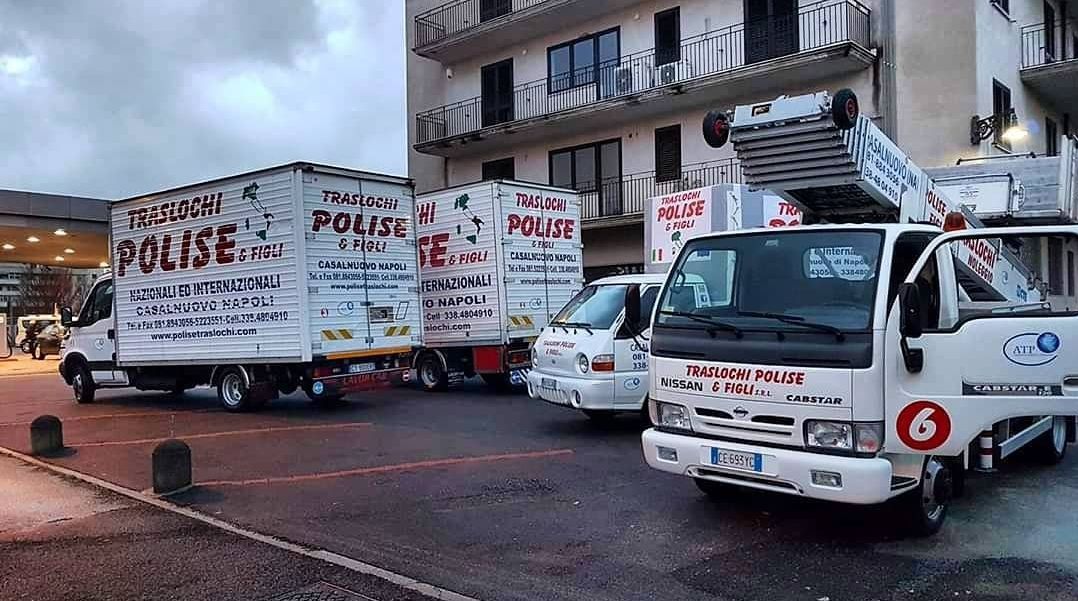 Veicoli di emergenza rossi e bianchi e un'autoscala parcheggiati davanti a un edificio su una strada bagnata al crepuscolo.