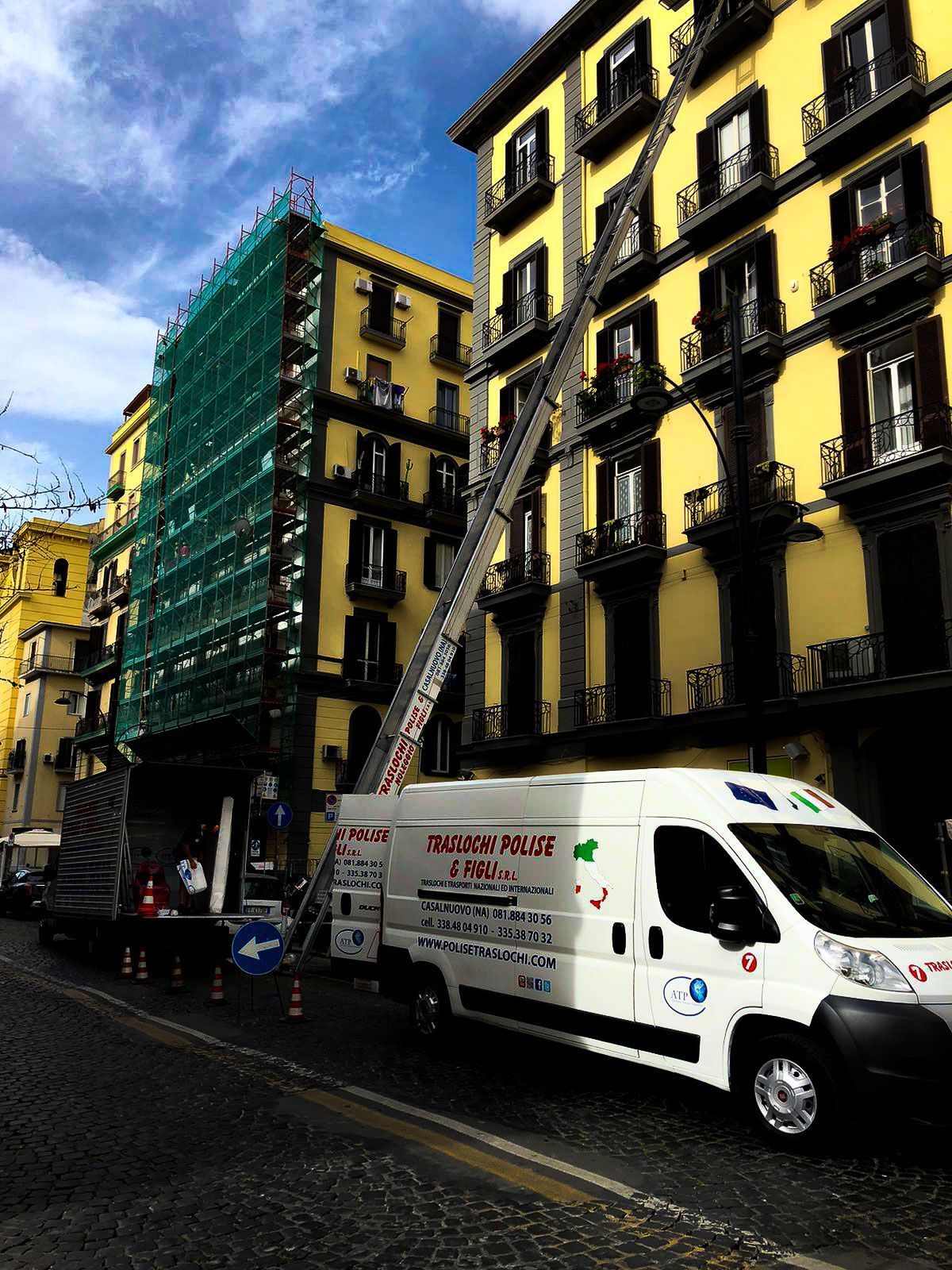 Scena di strada con edifici gialli, impalcature verdi e un furgone bianco parcheggiato su una strada stretta.