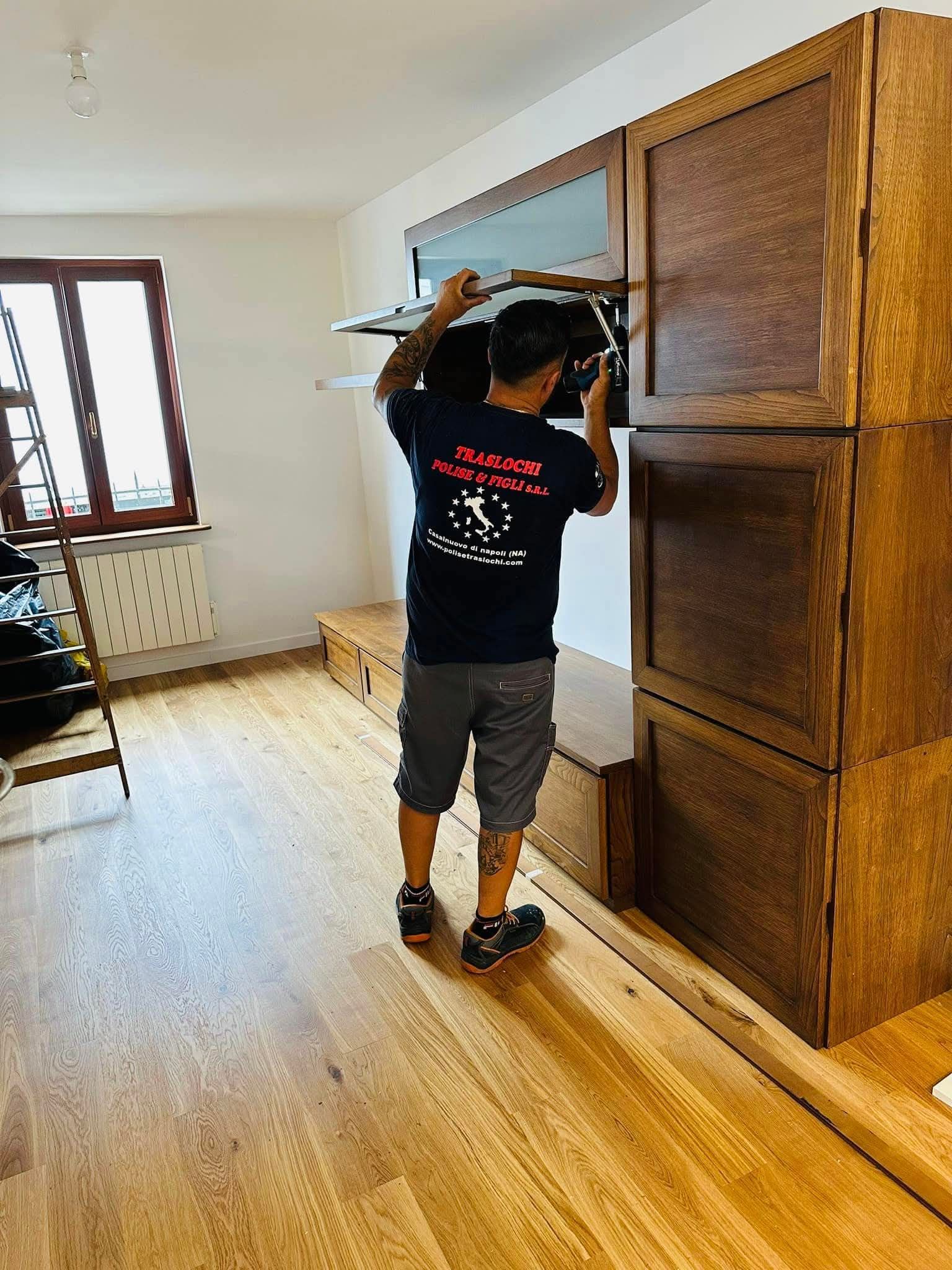 Una persona fruga in un armadio di legno in una stanza luminosa e perlopiù vuota.