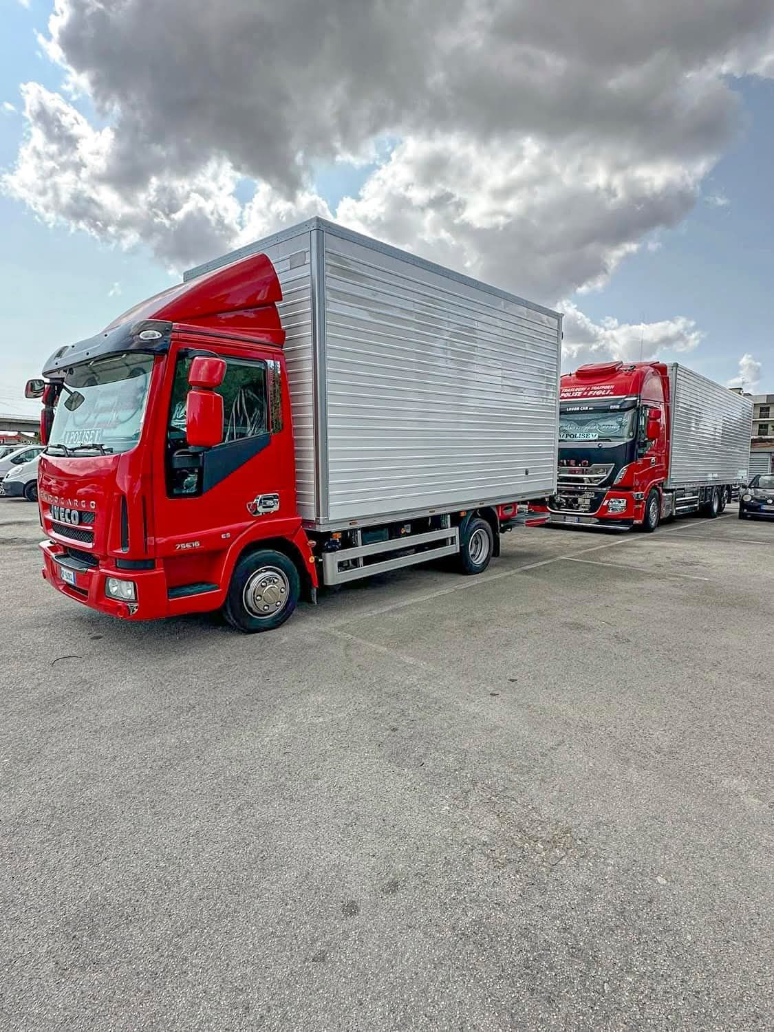 Due camion da carico rossi parcheggiati su un piazzale ghiaioso sotto un cielo nuvoloso