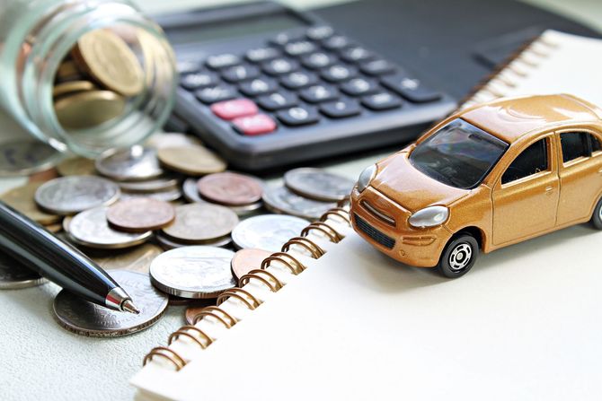 Un'auto giocattolo su un quaderno accanto a monete, calcolatrice e penna, a suggerire la pianificazione del budget o le spese per l'auto.