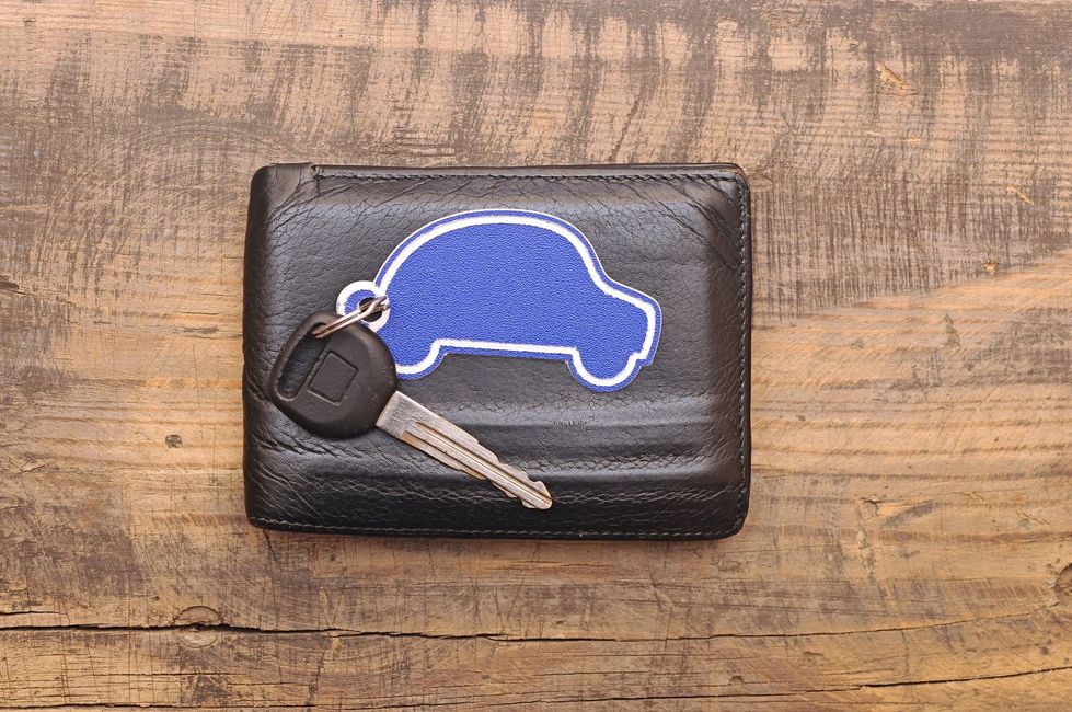 Portafoglio nero con chiave e toppa blu a forma di auto su una superficie in legno.