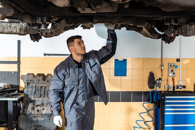 Un meccanico in tuta da lavoro ispeziona il sottoscocca di un'auto in un'officina meccanica.