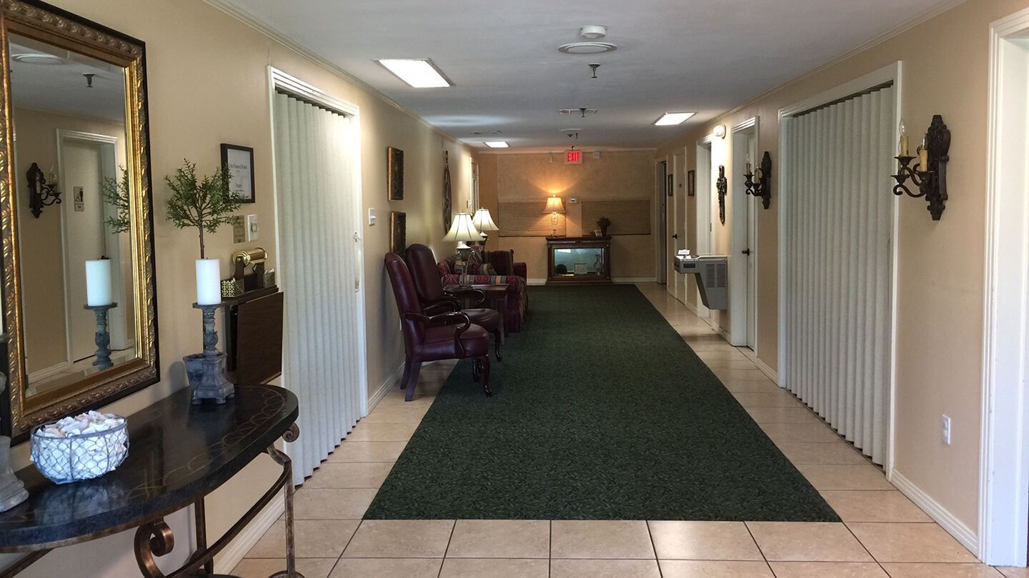Long hallway in a building with tiled floor, green carpet runner, chairs, mirrors, and wall sconces.