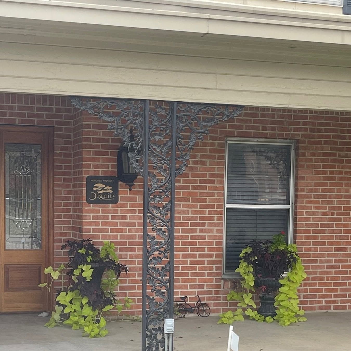 Brick house porch with wooden door, black mailbox, hanging lantern, and potted green plants by the windows.