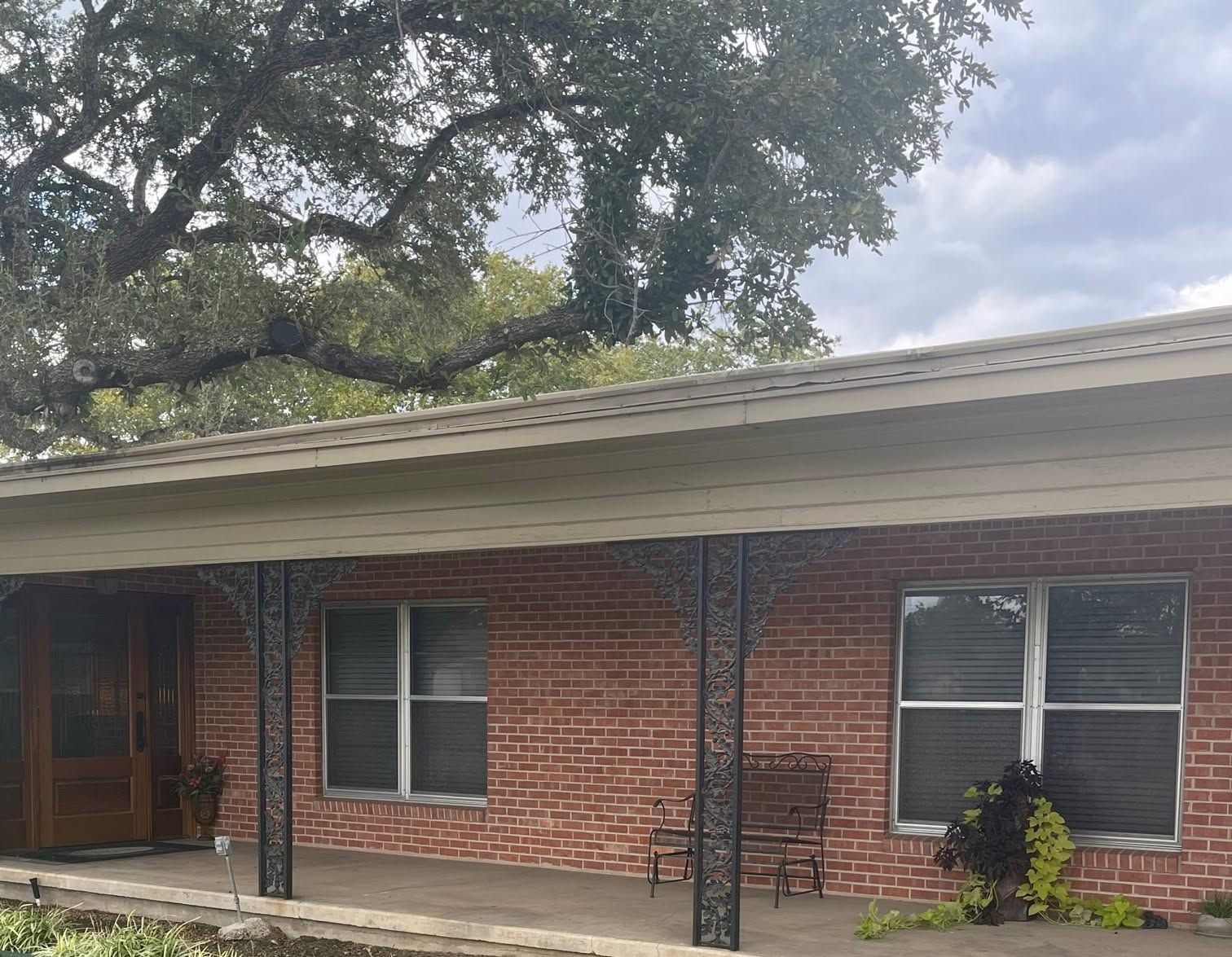 Brick house porch with white trim, black columns, and windows under trees
