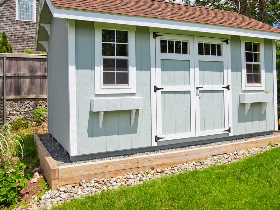 A blue and white shed with a brown roof is sitting on top of a lush green lawn.