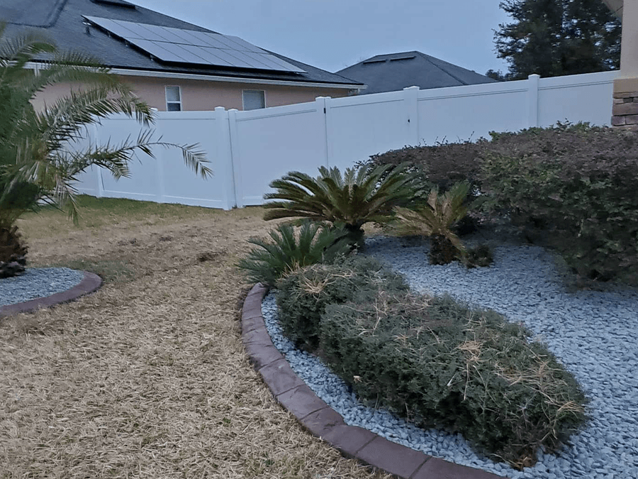 A garden with a white fence and a house in the background