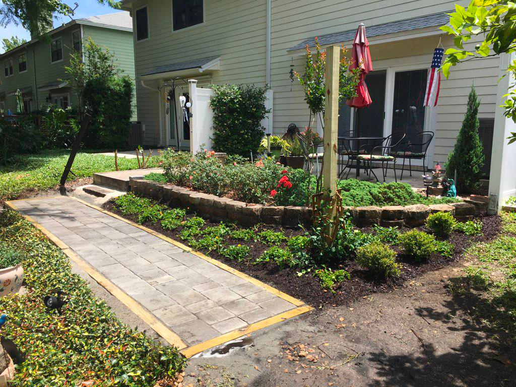 A walkway leading to a house with a garden in front of it.
