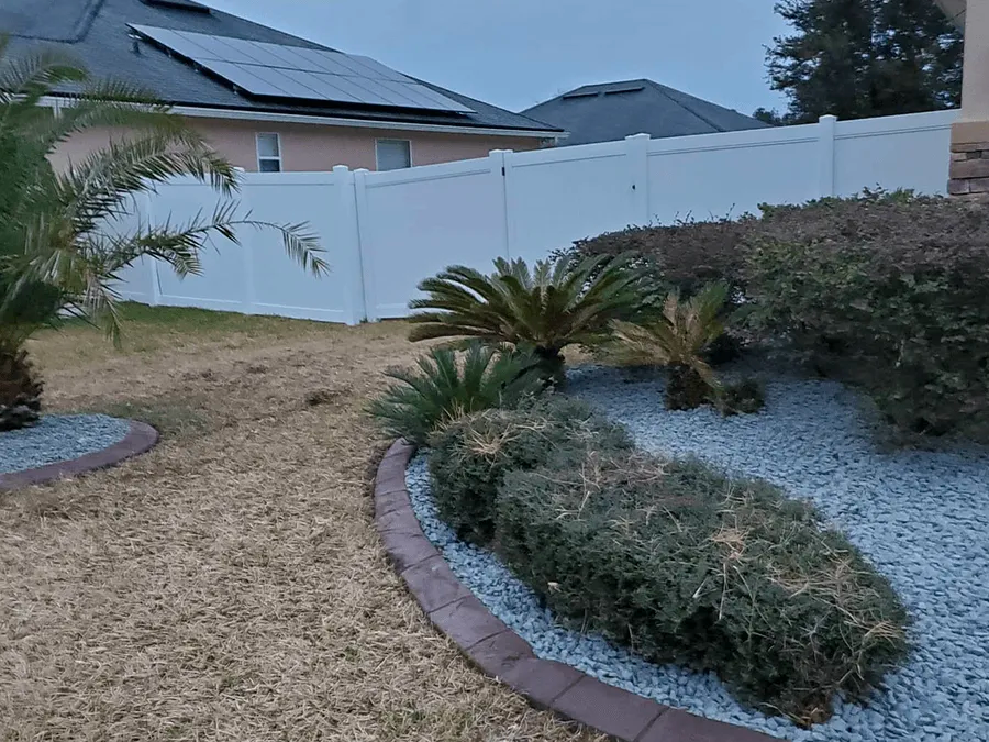 A garden with a white fence and a house in the background