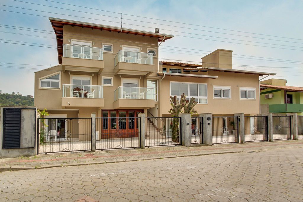 Prédio bege de vários andares com varandas, guarda-corpos de vidro e entrada com portão.