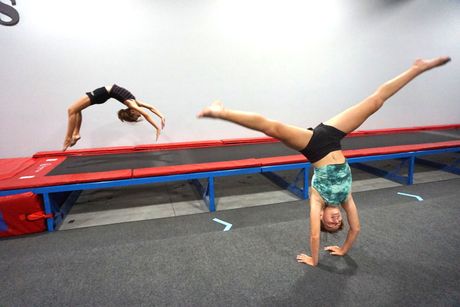 Two young girls are doing handstands on a trampoline.