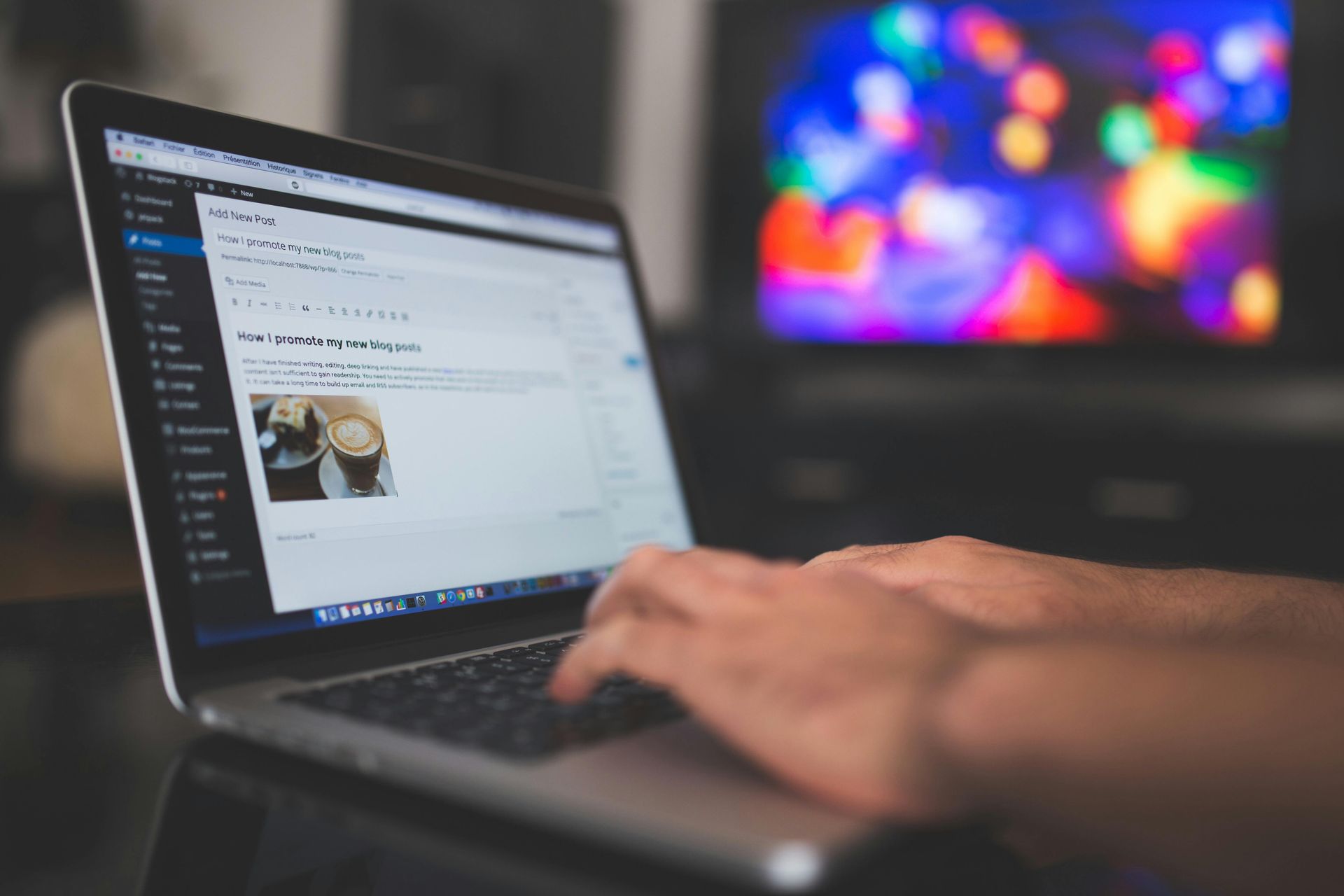 A person is typing on a laptop computer with a tv in the background.