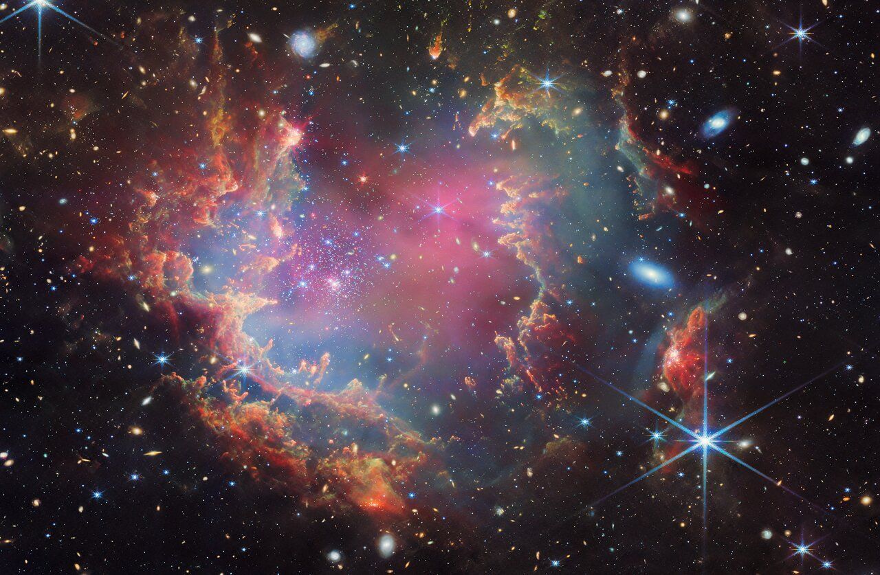 Colorful nebula with pink and blue hues, surrounded by dark space and many distant stars.