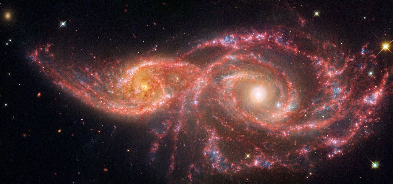 Two spiral galaxies in a collision, orange and red, in deep space.