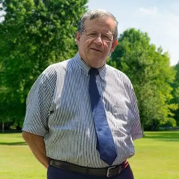 A man in a striped shirt and tie is standing in a park.