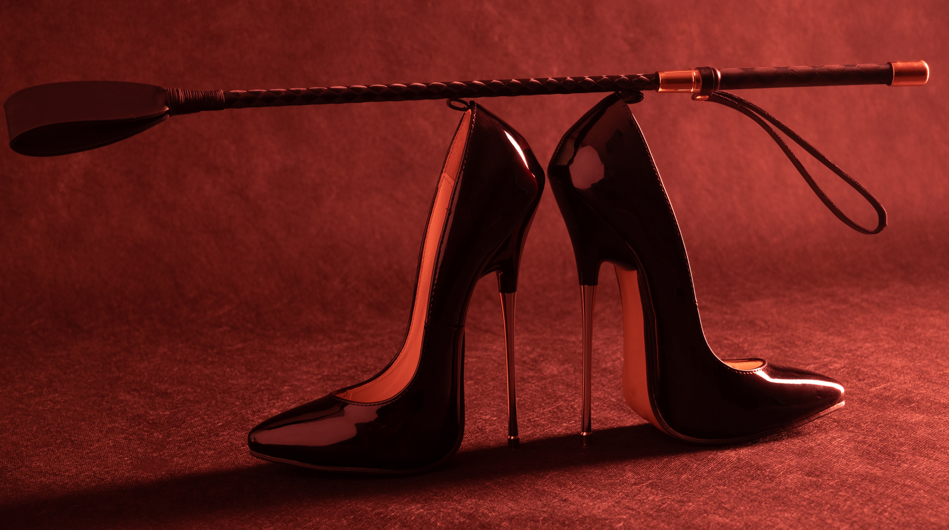Pair of black high-heeled shoes on a red background, with a paddle balancing across them