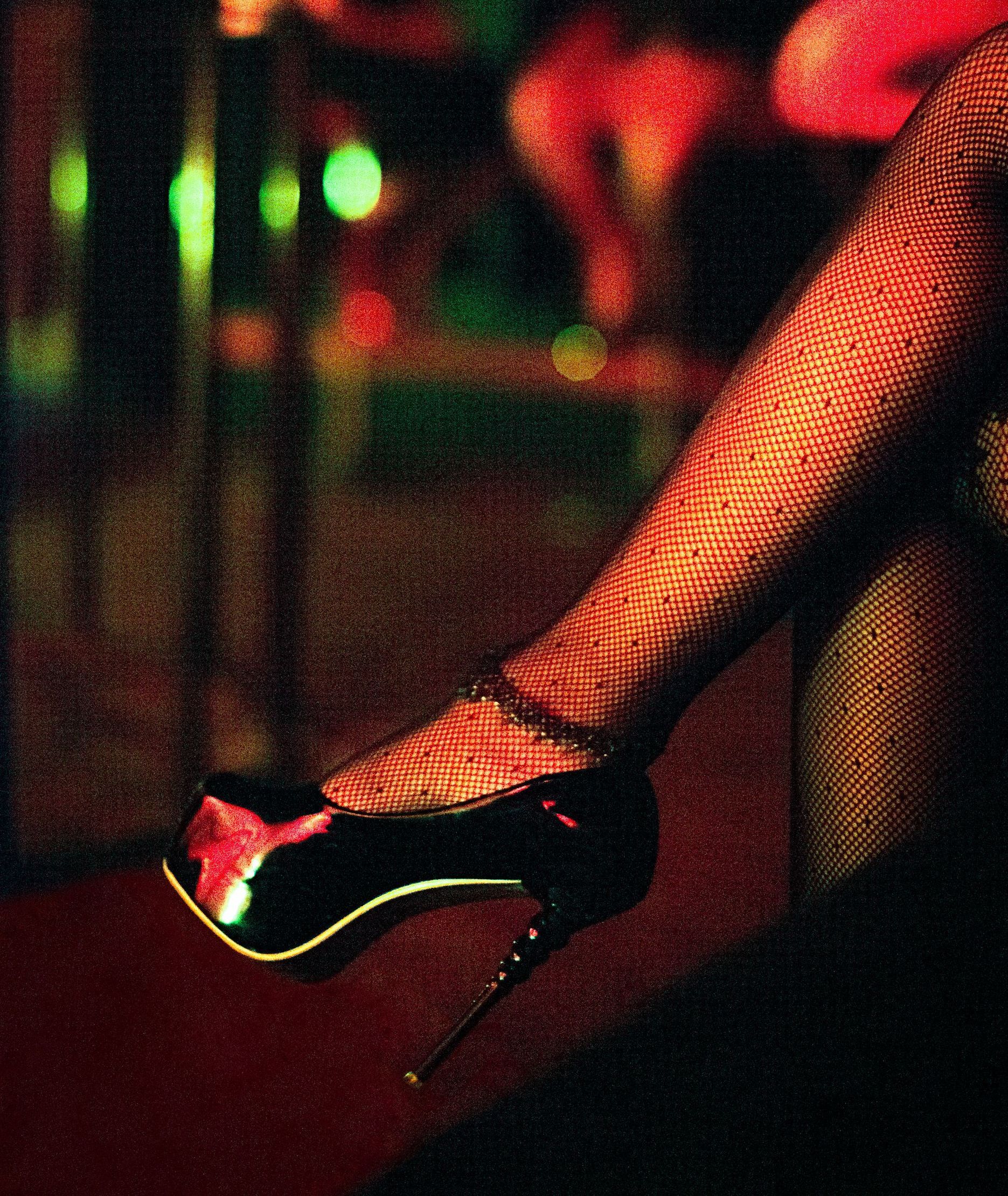A dancer’s leg in fishnet stockings and black high heel, lit by colorful club lights.