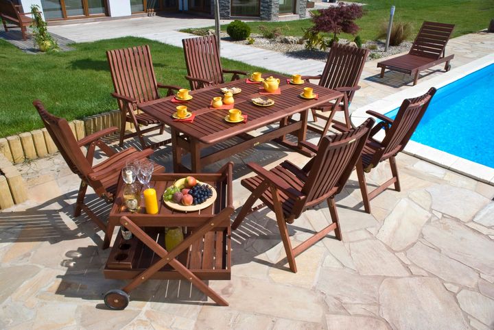 Set da pranzo per esterni: tavolo e sedie in legno marrone con rinfreschi, accanto a una piscina.