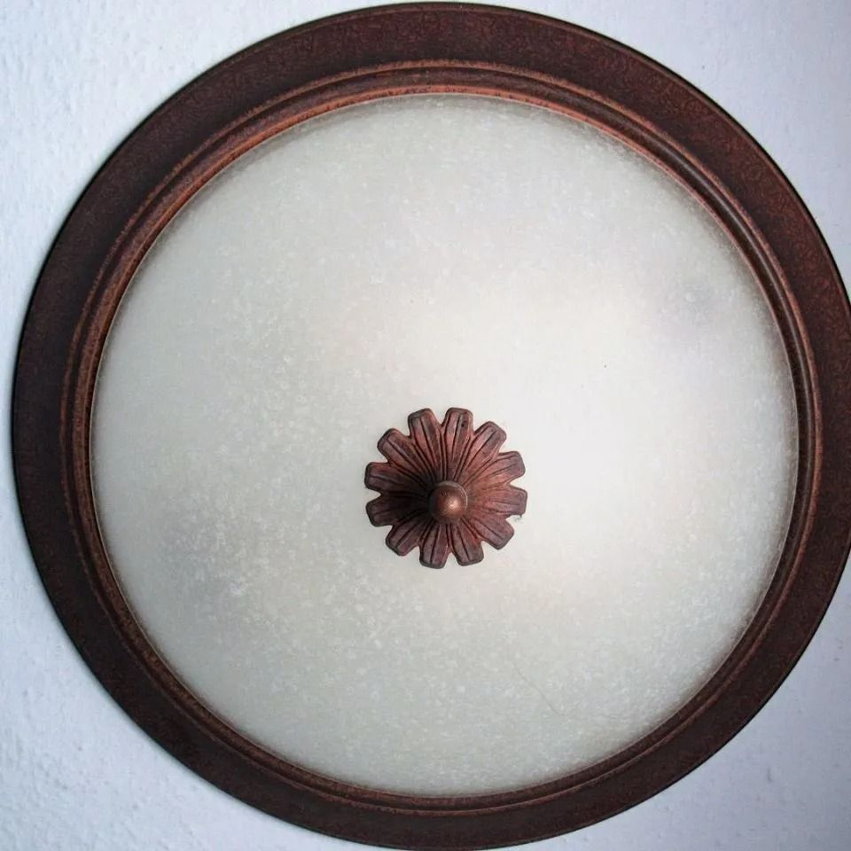 Lampada da soffitto con paralume in vetro smerigliato, circondata da una struttura in metallo color ruggine.