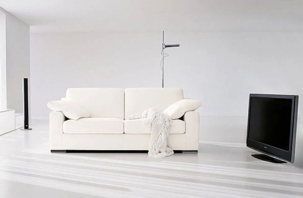 Divano bianco e TV in una stanza minimalista e bianca. Sono presenti anche altoparlanti alti e una lampada.