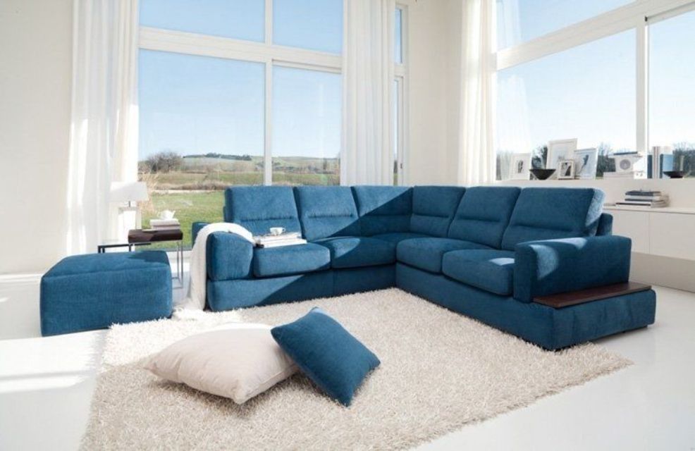 Divano componibile blu con pouf e cuscini decorativi in un luminoso soggiorno con ampie finestre e luce solare.