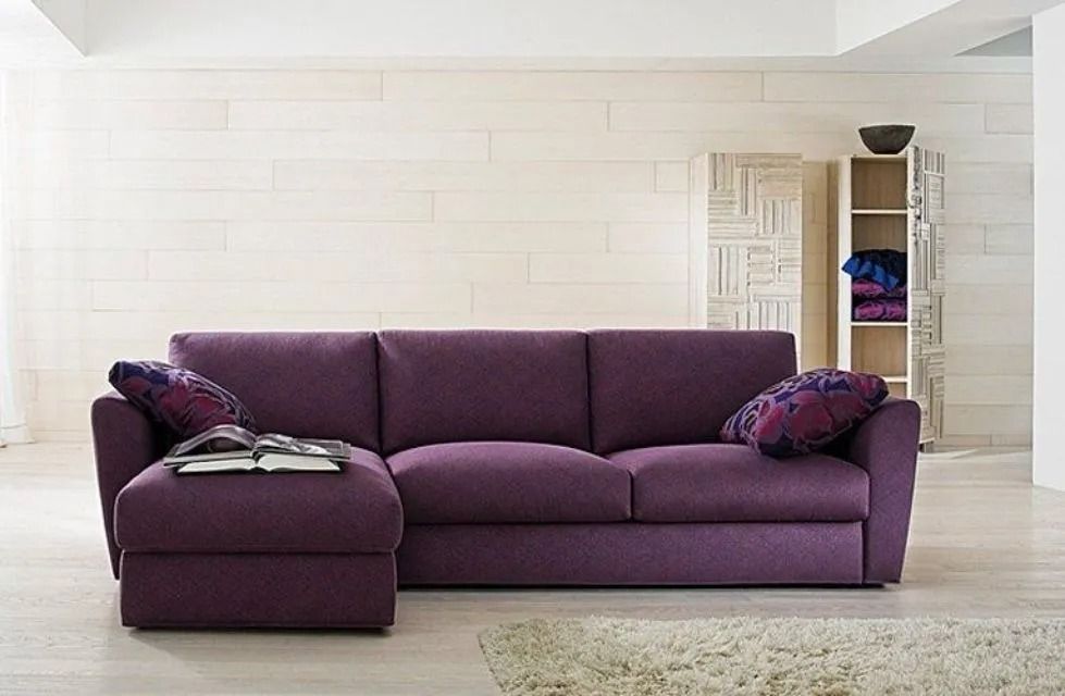 Divano componibile viola in una stanza luminosa con cuscini a fantasia e un tappeto neutro.