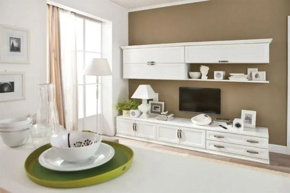 Mobili bianchi per il soggiorno disposti contro una parete marrone; includono una TV, contenitori e oggetti decorativi.
