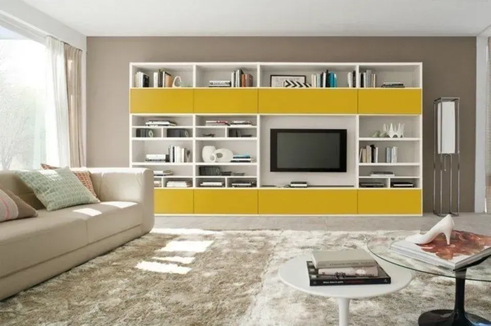 Soggiorno con un grande centro di intrattenimento integrato bianco e giallo, divano, tavolino da caffè e tappeto.