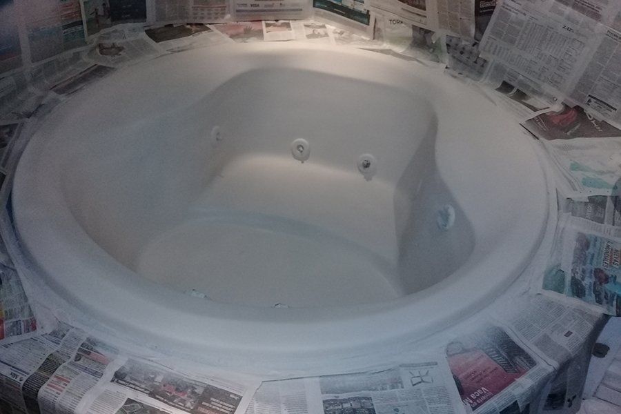 Bañera blanca recién imprimada rodeada de papel de periódico y cinta adhesiva durante los trabajos de restauración.