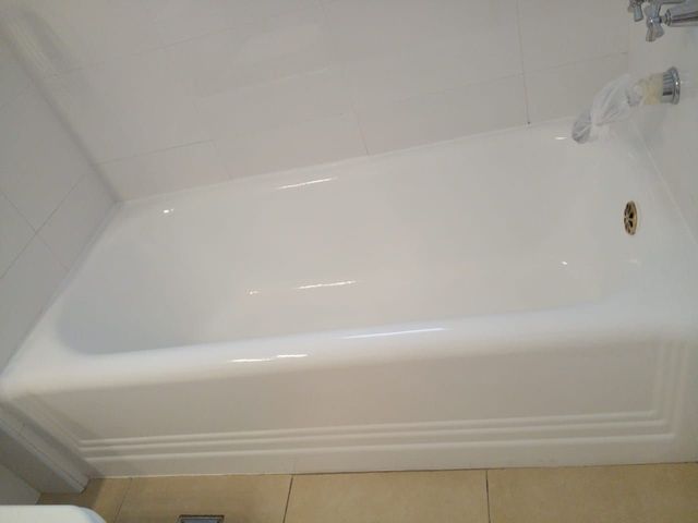 Bañera blanca con grifo cromado sobre paredes de baño de azulejos claros.