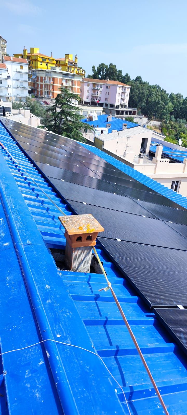 Pannelli solari blu sul tetto accanto a una piccola cassetta di legno, con vista su un quartiere collinare